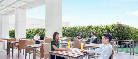 An outdoor seating area with tables and chairs, a clear sky, and a view of greenery.