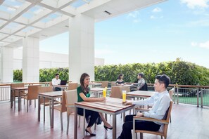 An outdoor seating area with tables and chairs, a clear sky, and a view of greenery. - Holiday Inn Express Jakarta Pluit Citygate by IHG (Jakarta)