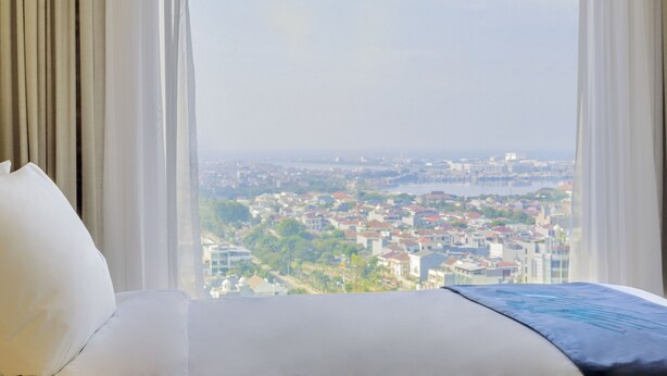 Une chambre d’hôtel avec un grand lit, des rideaux blancs et une vue sur le paysage urbain par la fenêtre.