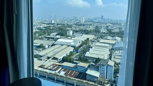 Une vue depuis une fenêtre donnant sur un paysage urbain, avec des bâtiments industriels et une ligne d’horizon lointaine.