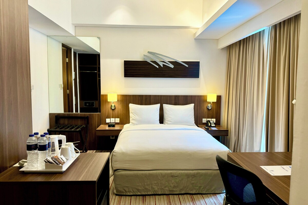 A hotel room with a large bed, two bedside tables with lamps, a desk with a tray of toiletries, and a mirror on the wall.