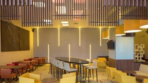 A modern hotel lobby with multiple seating areas, including round tables and chairs, and a high ceiling with vertical light fixtures. - Holiday Inn Express Jakarta Pluit Citygate by IHG (Jakarta)