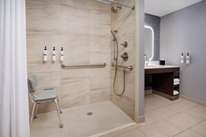 A modern bathroom with a walk-in shower, grab bars, a wheelchair-accessible chair, and a vanity with a mirror. - Homewood Suites by Hilton Midland, TX (Midland)