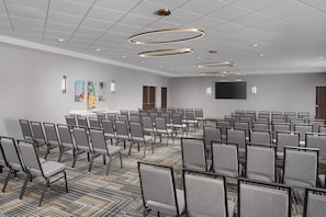 A conference room with rows of chairs, a carpeted floor, a flat-screen TV, and a ceiling with circular light fixtures. - Homewood Suites by Hilton Midland, TX (Midland)