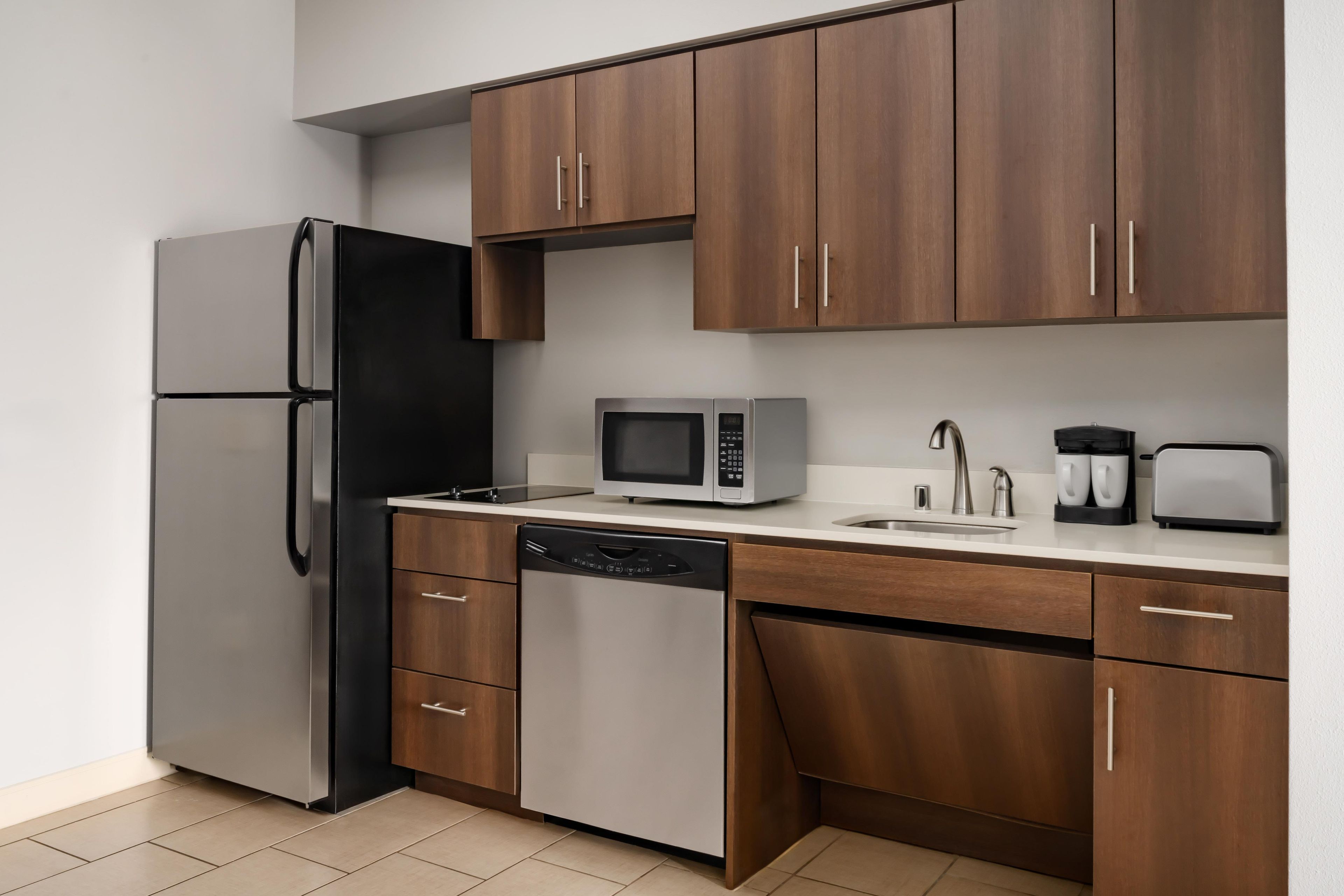 A kitchen with a refrigerator, microwave, dishwasher, and wooden cabinets.