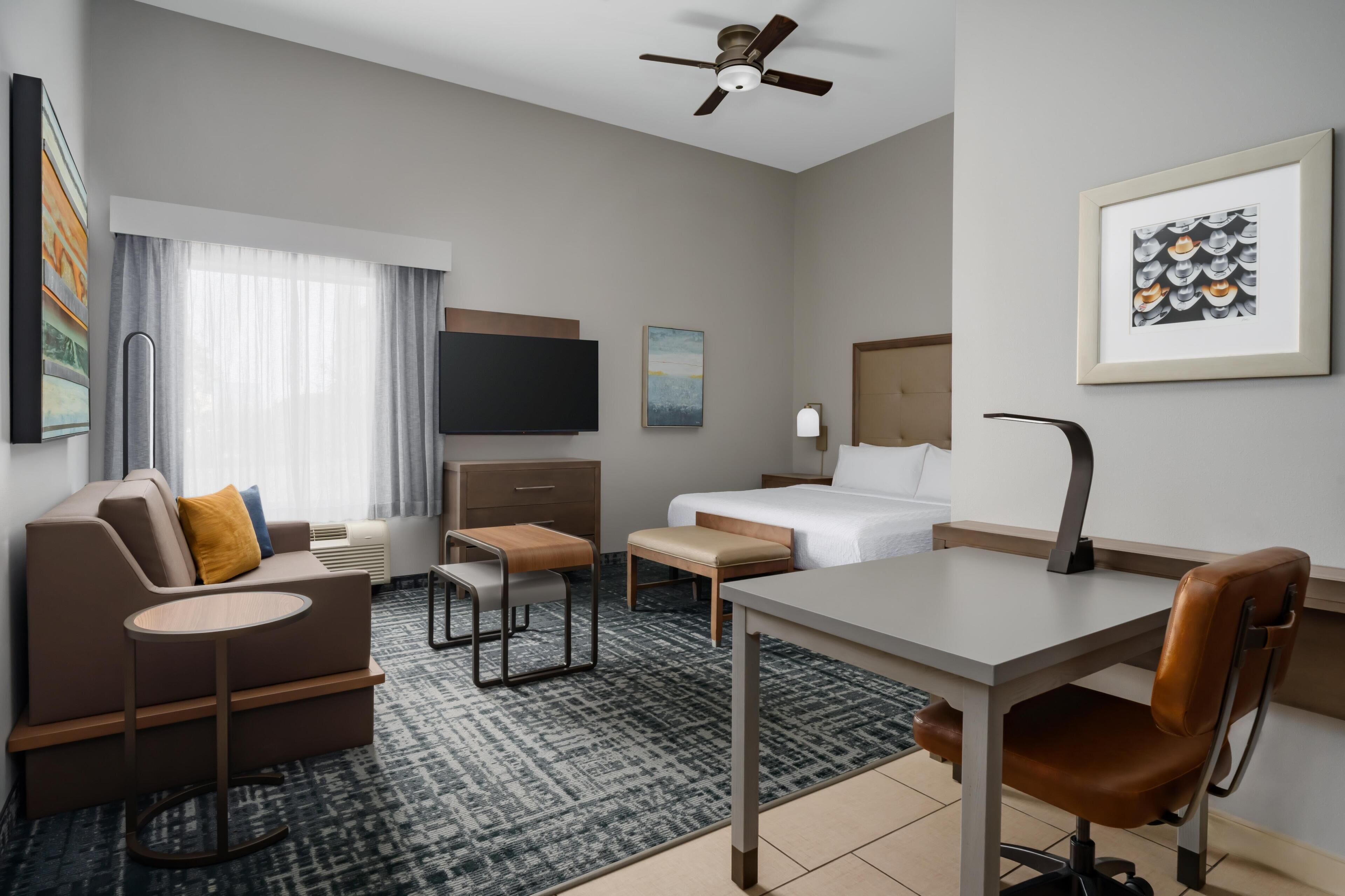A hotel room with a bed, a desk, a sofa, a TV, and a ceiling fan.