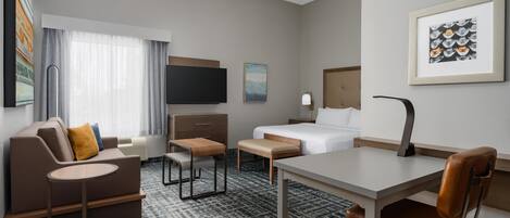 A hotel room with a bed, a desk, a sofa, a TV, and a ceiling fan.