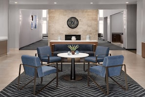 A lobby with a round table, four blue chairs, a clock, and a fireplace. - Homewood Suites by Hilton Midland, TX (Midland)