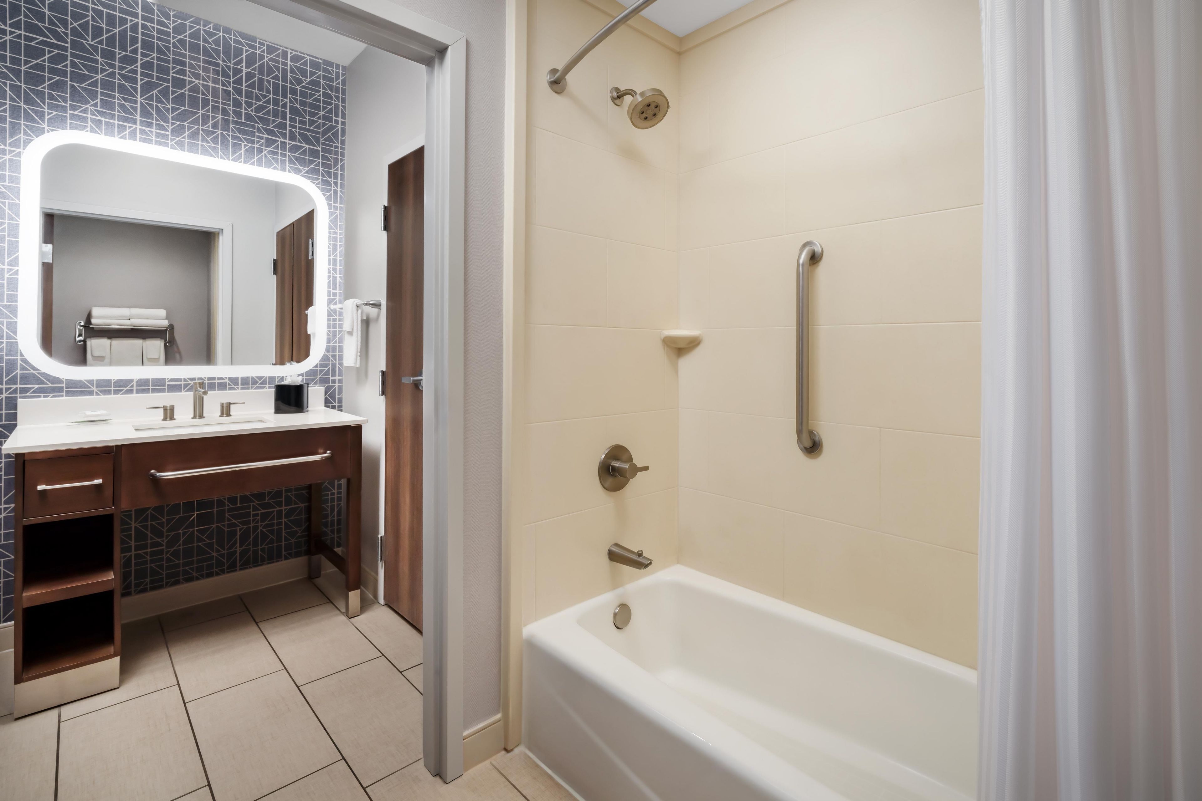 A modern bathroom with a white bathtub, a large mirror, a vanity with a sink, and a shower area.