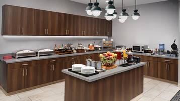 A modern kitchen with dark wooden cabinets, a central island with fruit, and various appliances.