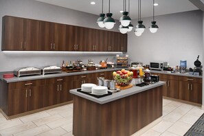A modern kitchen with dark wooden cabinets, a central island with fruit, and various appliances. - Homewood Suites by Hilton Midland, TX (Midland)