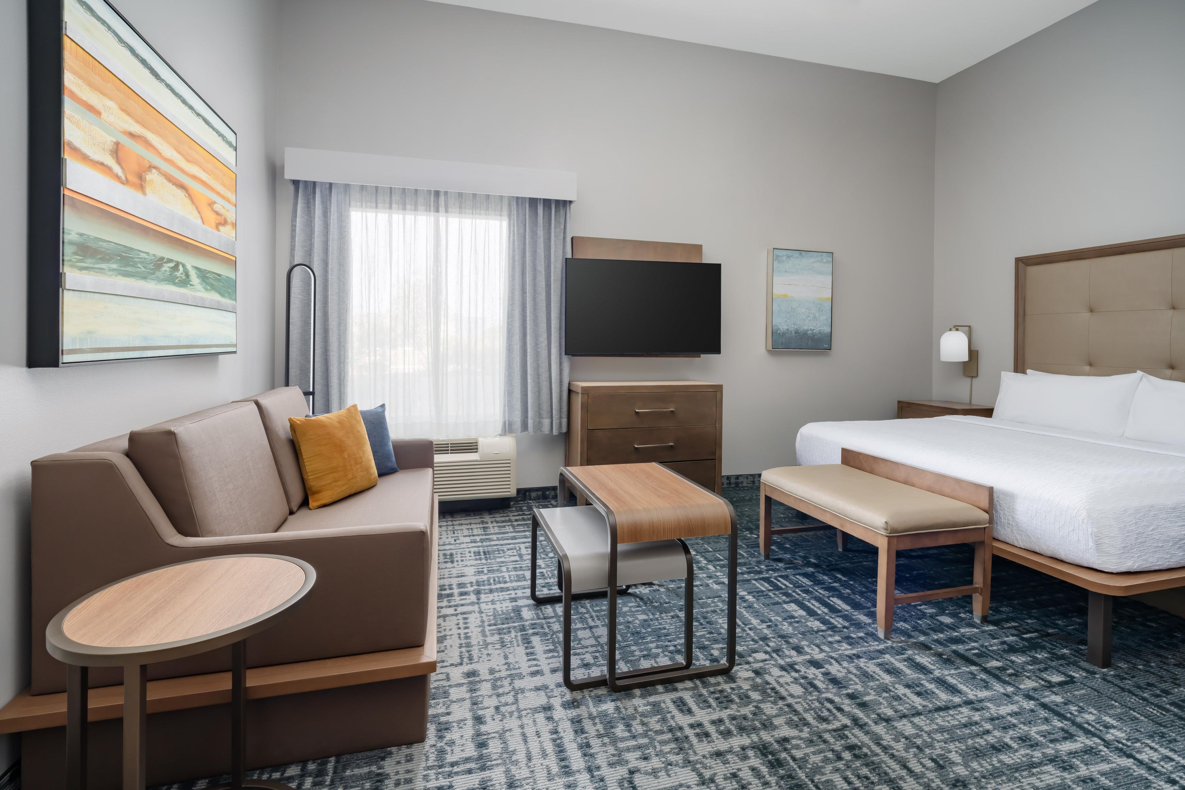 Een hotelkamer met een bed, een bank, een bureau, een televisie en een raam met gordijnen.