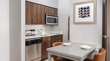 Une cuisine moderne équipée d’un four à micro-ondes, d’un four et d’un lave-vaisselle, une table à manger avec des chaises, et un tableau encadré au mur.