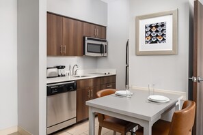 A modern kitchen with a microwave, oven, and dishwasher, a dining table with chairs, and a framed picture on the wall. - Homewood Suites by Hilton Midland, TX (Midland)