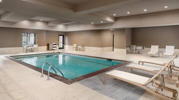 A swimming pool with lounge chairs and a sunbed, surrounded by a tiled floor and a neutral color scheme.