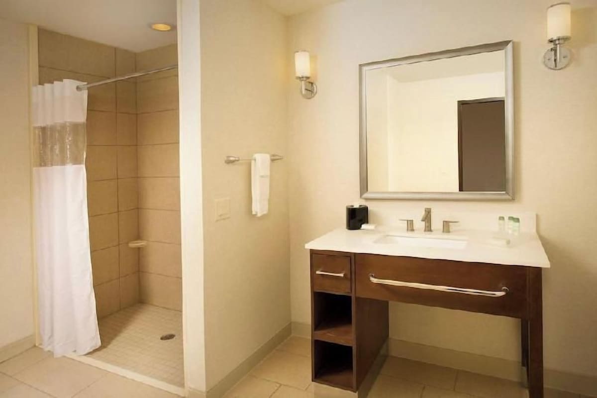 A bathroom with a shower, a sink, a mirror, and a towel rack.