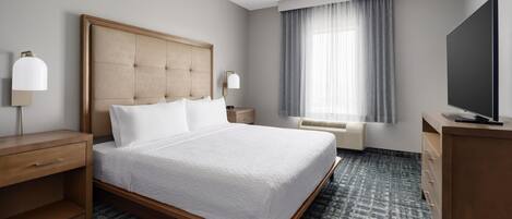A hotel room with a large bed, a desk, a television, a ceiling fan, a window with curtains, and a wall-mounted TV.