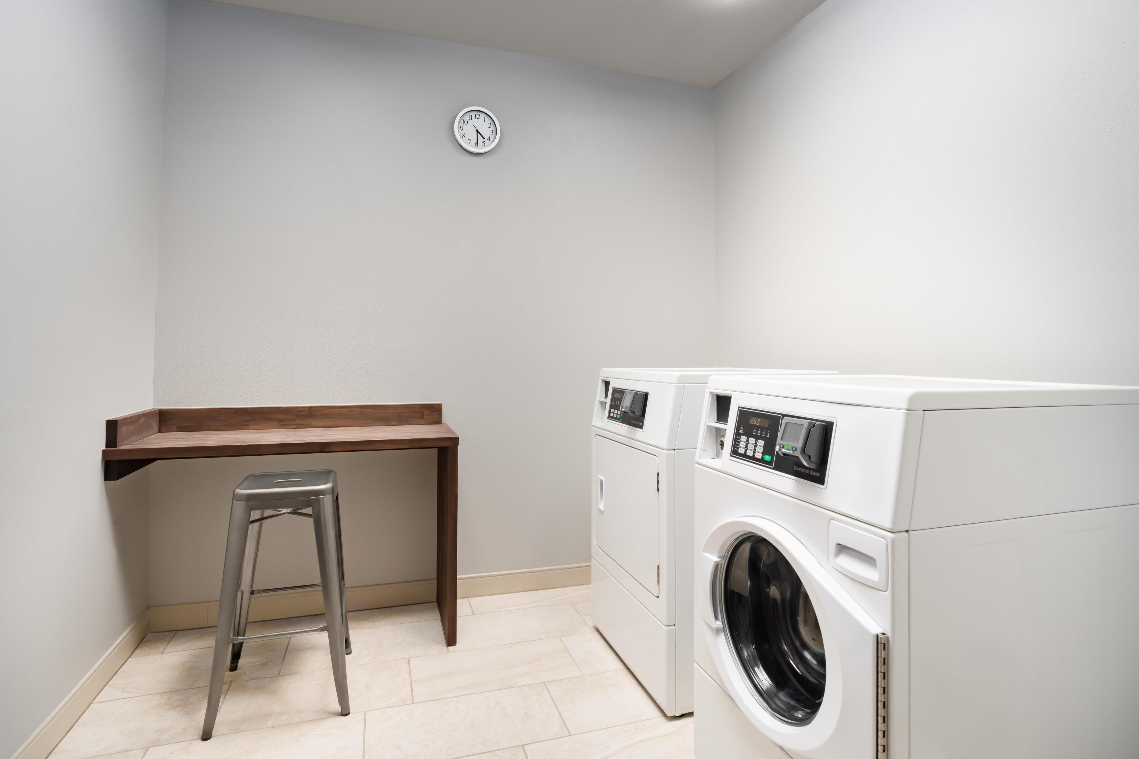 A laundry room with a washing machine, a dryer, a wooden bench, and a stool.