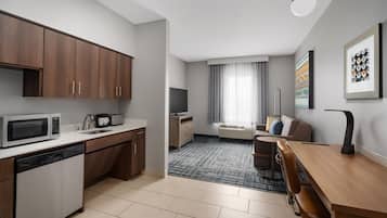 A modern kitchen with a dishwasher, microwave, and a flat-screen TV. There's a dining area with a wooden table and chairs, and a living space with a sofa and a TV.