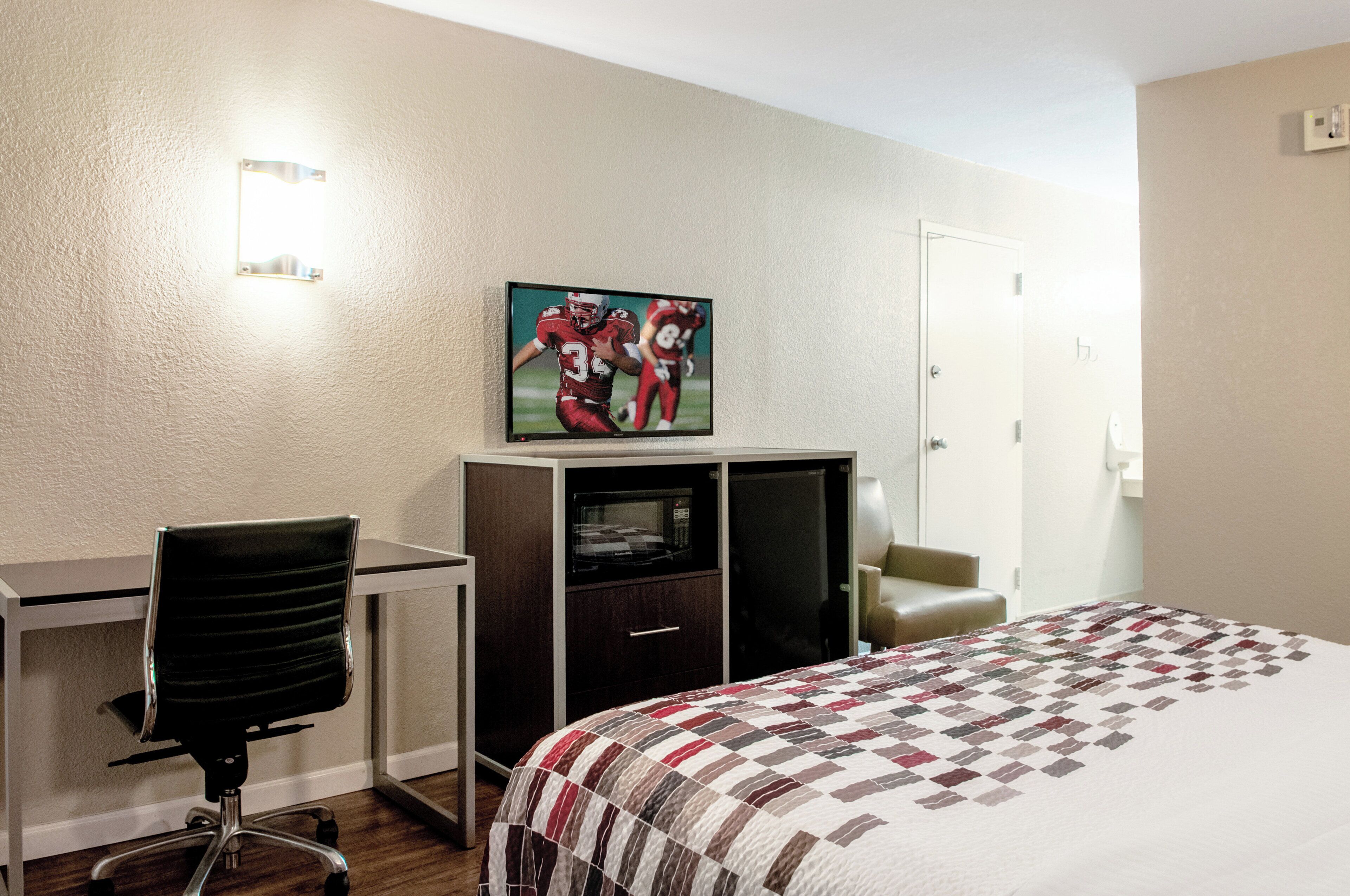Una habitación de hotel con cama, escritorio, silla, televisor y un cuadro en la pared.