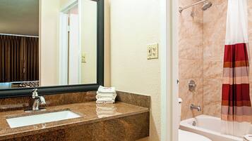 A bathroom with a granite countertop sink, a mirror, a shower with a striped curtain, and a bathtub.