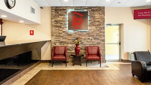A Red Roof Inn reception area with a stone wall, two leather chairs, a clock, and a sign indicating free Wi-Fi in all rooms. - Red Roof Inn Slidell  (Slidell)
