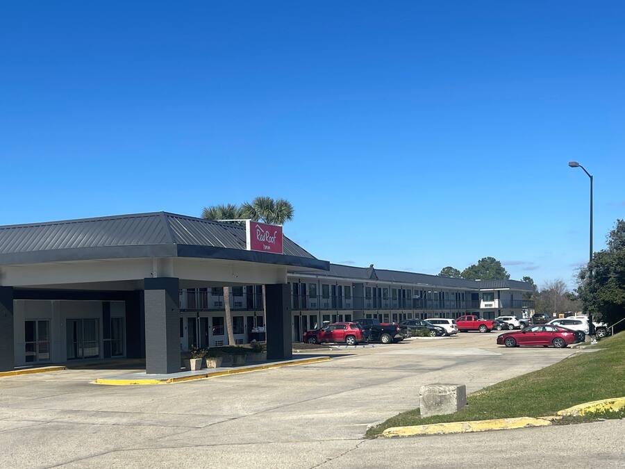 A Red Roof Inn with a modern design, featuring a flat roof and a parking lot with several cars.