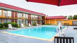 A swimming pool area with lounge chairs and umbrellas, a building with multiple windows and balconies, and a fenced yard. - Red Roof Inn Slidell  (Slidell)