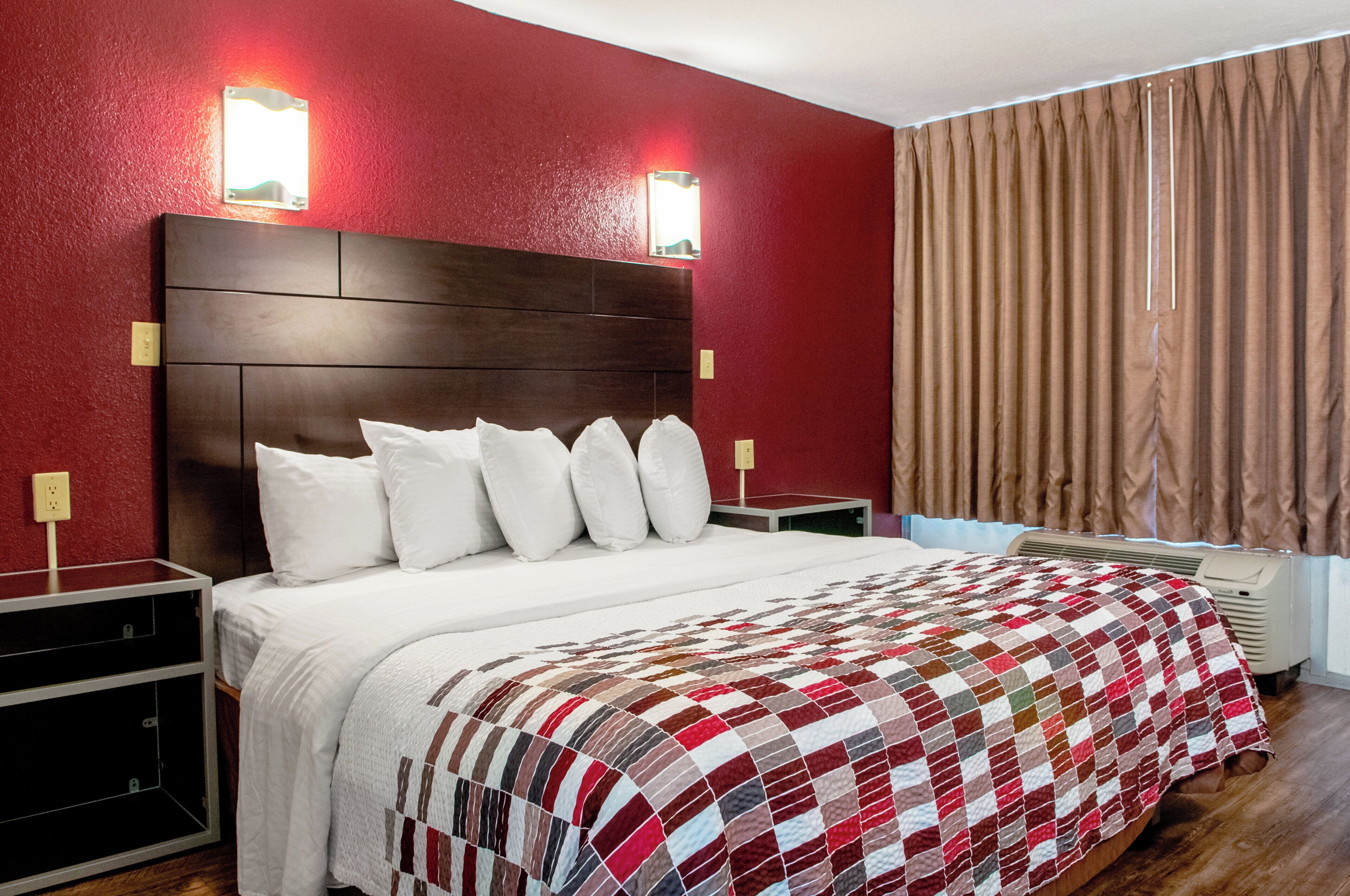 A hotel room with a large bed, a wooden headboard, and a red wall.