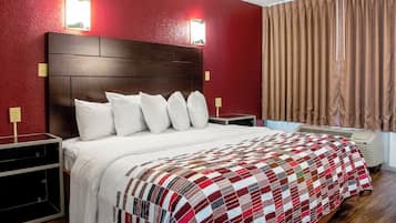 A hotel room with a large bed, a wooden headboard, and a red wall.