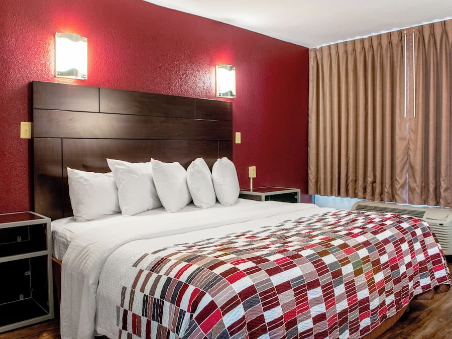 A hotel room with a large bed, a wooden headboard, and a red wall.