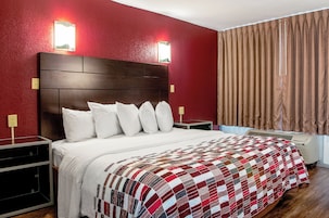 Habitación de hotel con una cama grande, cabecero de madera y pared roja.