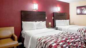 Une chambre d’hôtel avec deux lits, une chaise et un mur rouge.