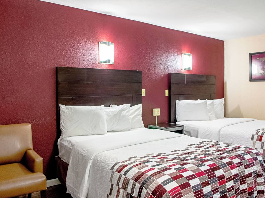 A hotel room with two beds, a chair, and a red wall.