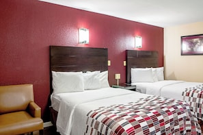 A hotel room with two beds, a chair, and a red wall.
