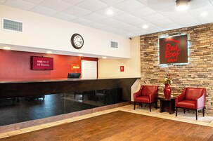 Una zona de recepción con un reloj, un letrero de Red Roof Inn y dos sillas rojas.
