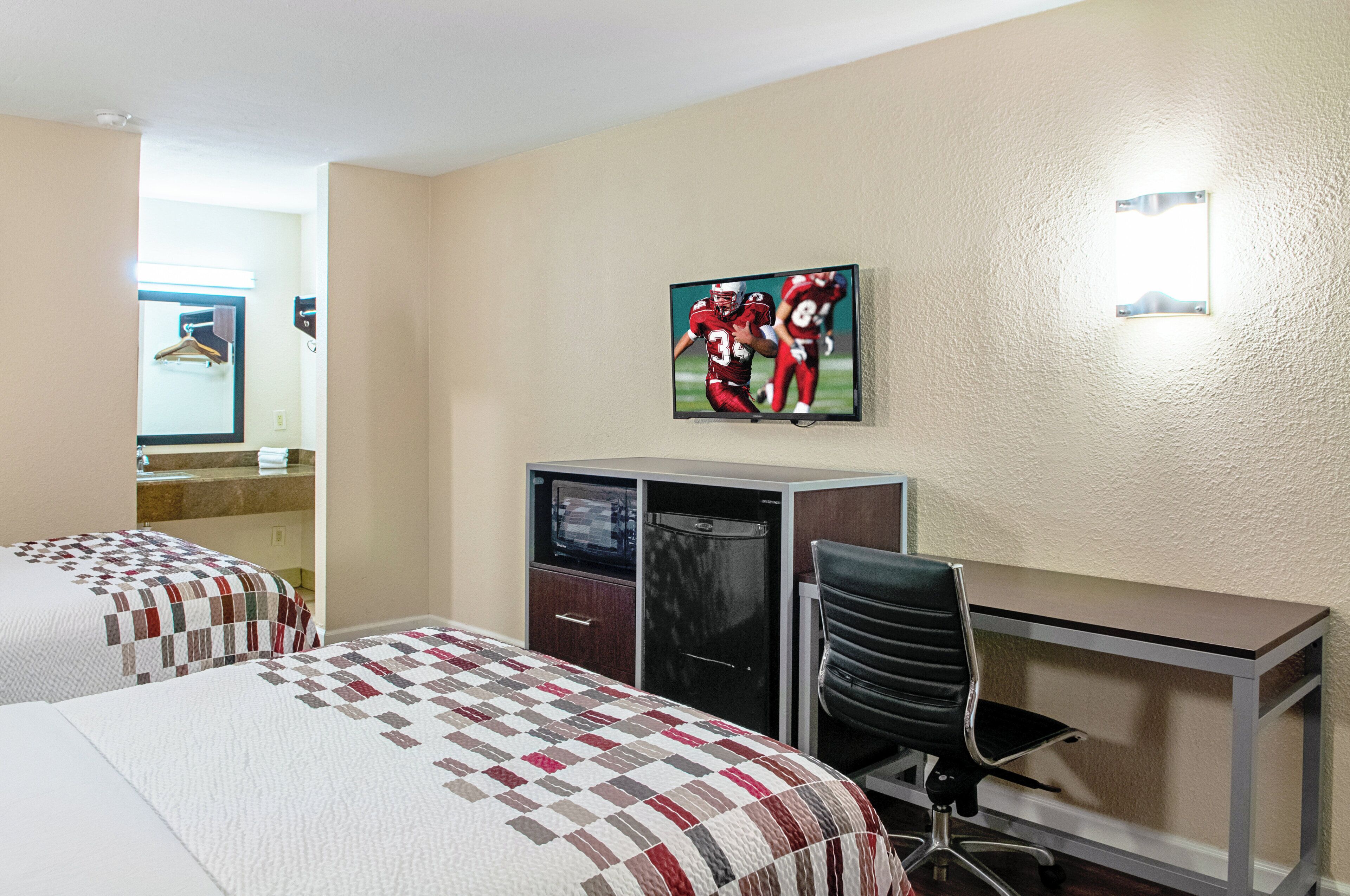 Ein Hotelzimmer mit zwei Betten, einem Schreibtisch, einem Sessel, einem Fernseher und einem Spiegel.