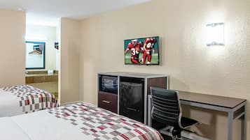 Ein Hotelzimmer mit zwei Betten, einem Schreibtisch, einem Sessel, einem Fernseher und einem Spiegel.
