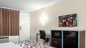 A hotel room with a bed, a desk, a chair, a television, and a wall-mounted picture.