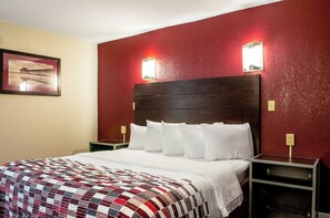 A hotel room with a large bed, a red accent wall, two bedside lamps, and a framed picture on the wall. - Red Roof Inn Slidell  (Slidell)