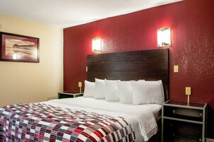 Una habitación de hotel con una cama grande, una pared de acento roja, dos lámparas de noche y un cuadro en la pared.