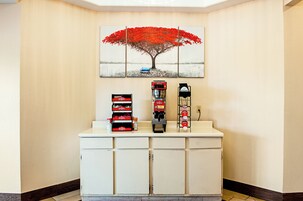 Un área de recepción con una máquina de café, un dispensador de bebidas y una pila de cajas rojas sobre un mostrador.