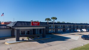 Un hôtel Red Roof Inn avec un parking, un drapeau et une rangée de bâtiments.