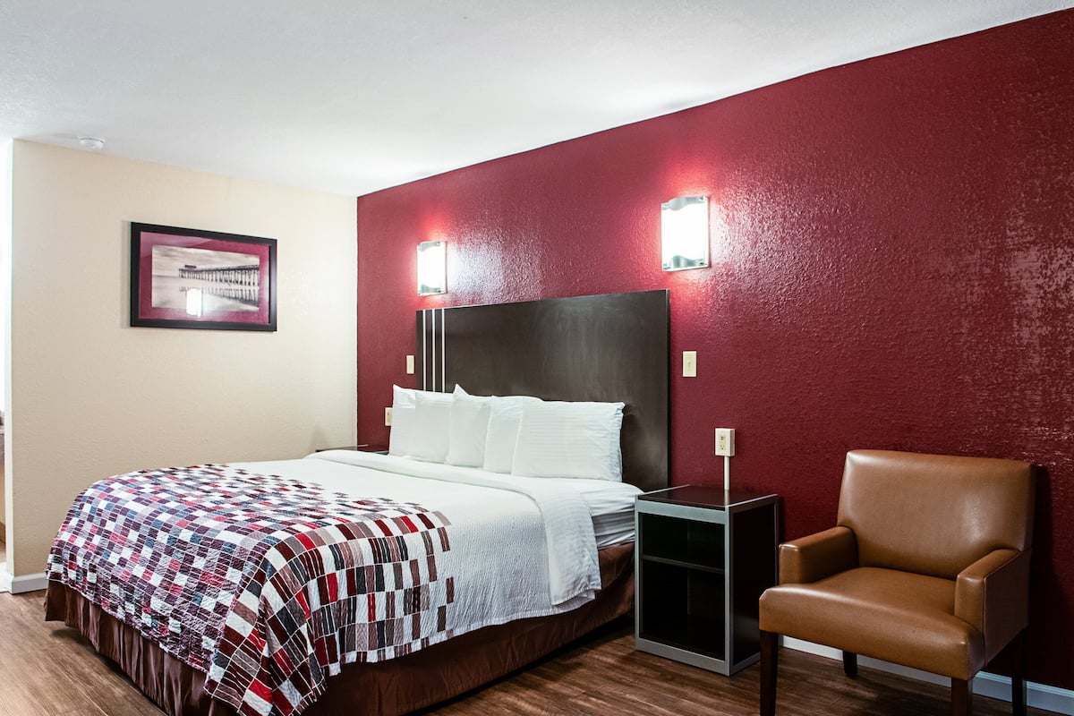 A hotel room with a large bed, a brown leather chair, and two wall-mounted lights.