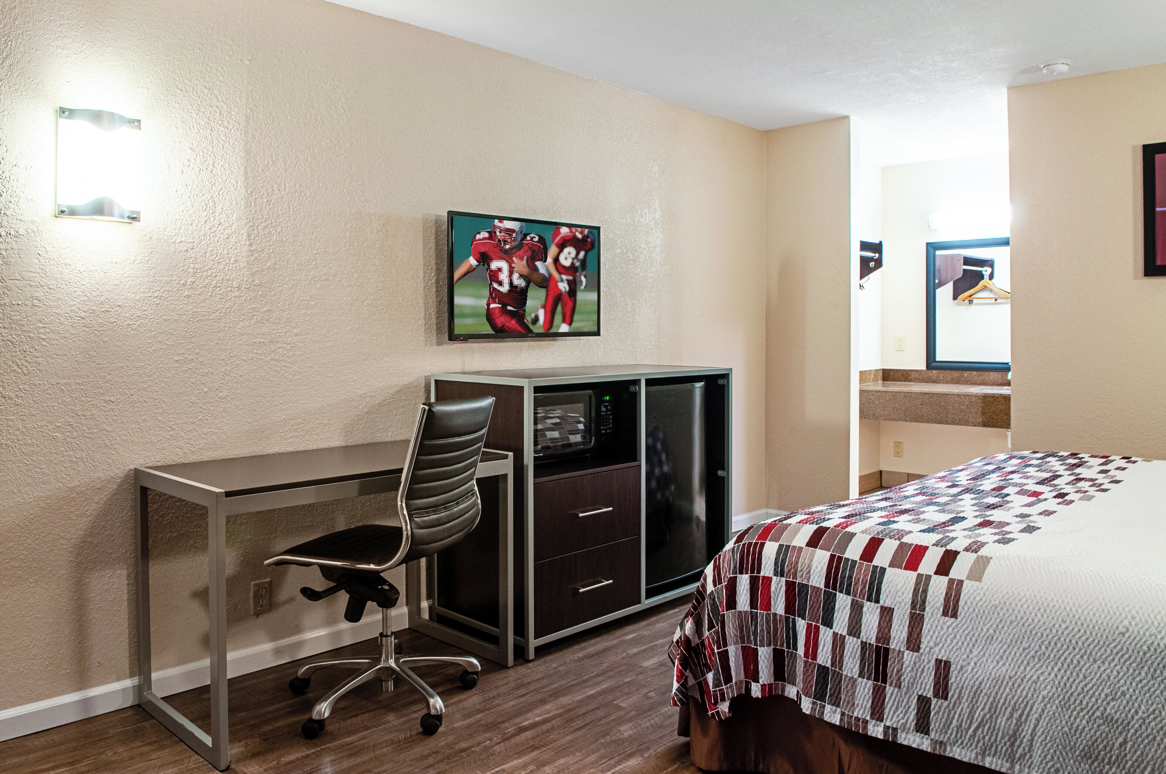 Ein Hotelzimmer mit Schreibtisch, Stuhl, Bett und einem an der Wand befestigten Fernseher.