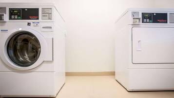Deux machines à laver à chargement frontal, de couleur blanche, se trouvent dans une pièce dont le mur est d’un blanc uni et dont le sol est carrelé.