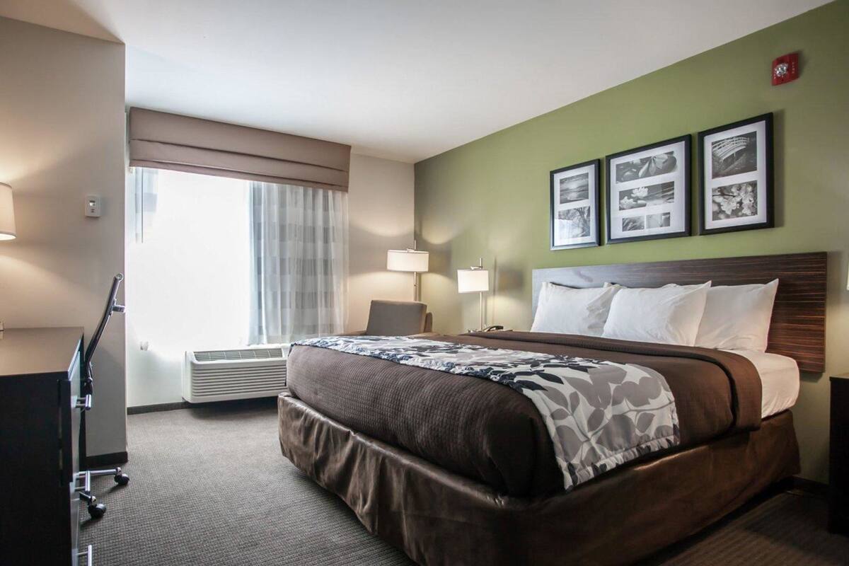 A hotel room with a large bed, a desk, and a chair. There are three framed pictures on the wall.