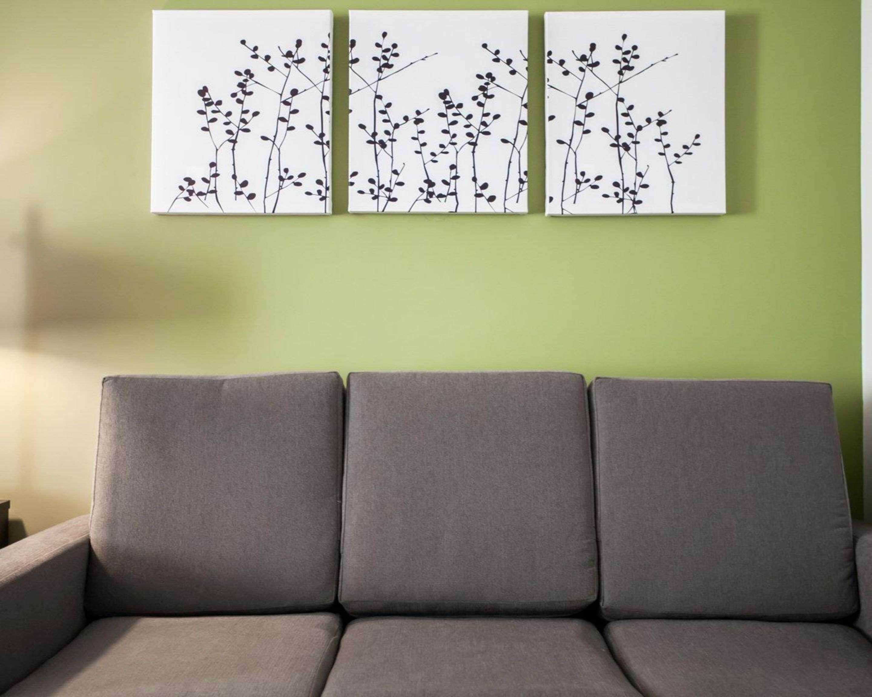 A grey sofa against a green wall with three white panels featuring black silhouettes of branches and leaves.