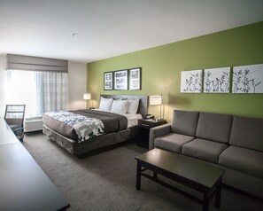 Habitación de hotel con cama, sofá, mesa de centro, escritorio y una silla. Hay tres cuadros en la pared.