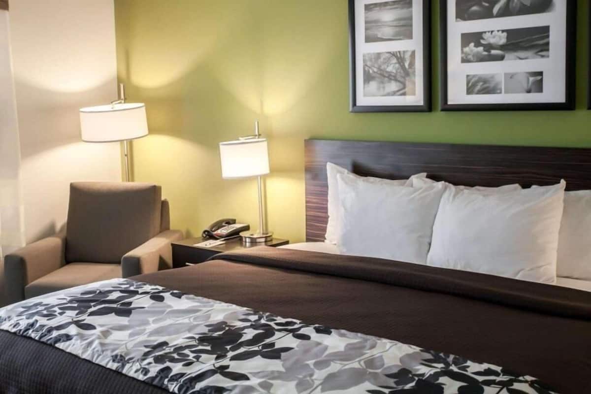 A hotel room with a bed, two bedside lamps, a chair, and two framed pictures on the wall.